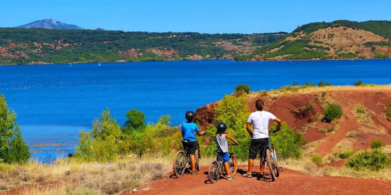 Famille à vélo profitant d'une randonnée au lac du Salagou, avec ses eaux bleues et ses collines rouges.