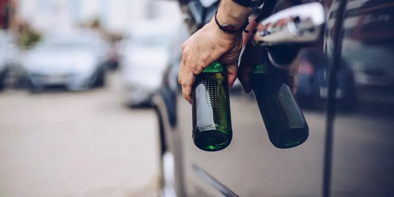 Mann hält zwei Bierflaschen aus dem Autofenster. Er versucht, den Alkohol abzubauen, indem er sie wegwirft.