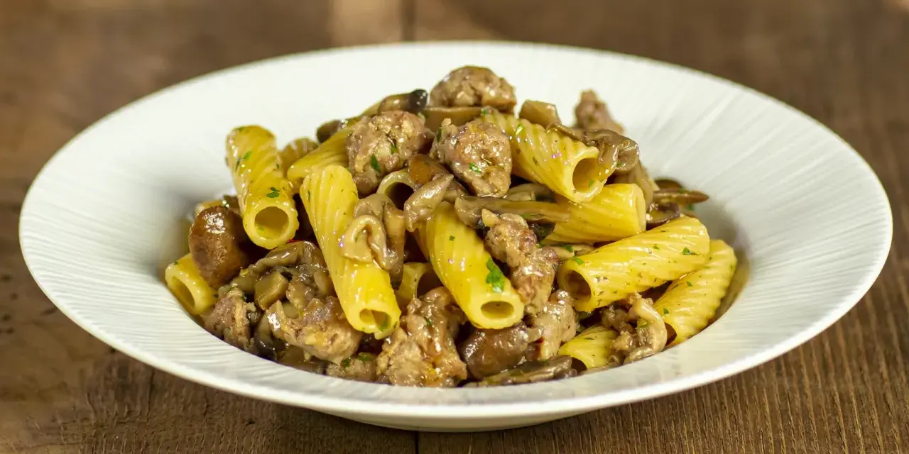 Piatto di pasta funghi e salsiccia, con rigatoni conditi con funghi trifolati e pezzetti di salsiccia saporita.