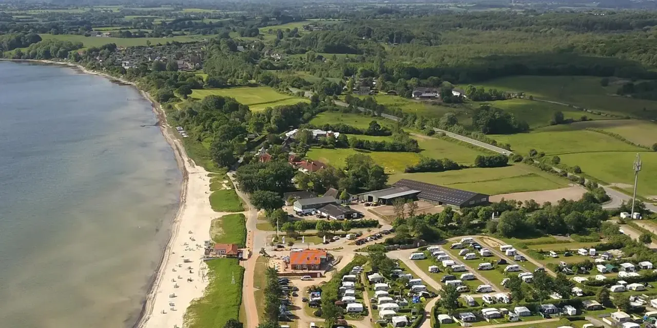 Luftaufnahme eines Campingplatzes in Schleswig-Holstein mit Wohnmobilen und Zelten, direkt am sandigen Strand und dem Meer gelegen.