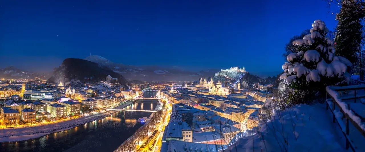 Magiczne salzburg zimą. Oświetlone miasto, rzeka Salzach i górująca twierdza Hohensalzburg w śnieżnej scenerii nocą.
