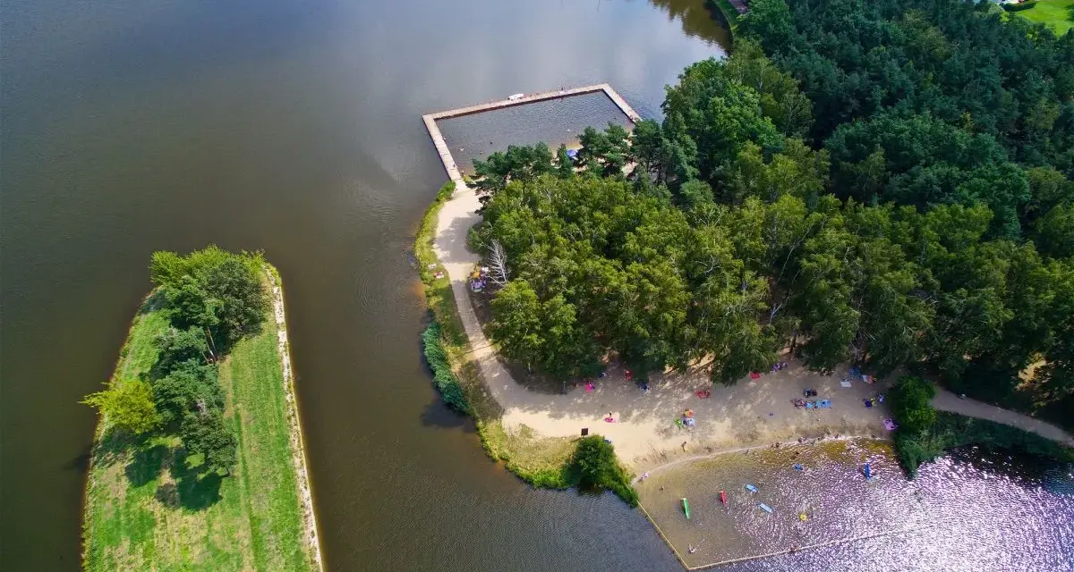 Widok z lotu ptaka na jezioro z kąpieliskiem, plażą i lasem.