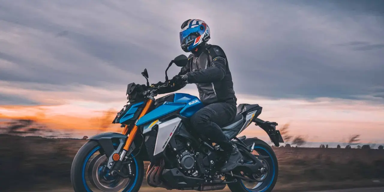 Motocyklista w kasku jedzie na niebieskim Suzuki GSX-S1000 podczas zachodu słońca.