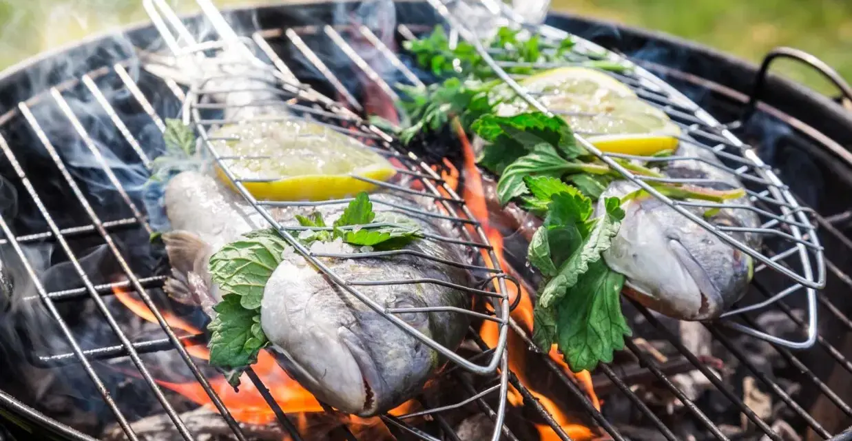 Dwie ryby na grillu, z cytryną i ziołami, unoszą się nad ogniem. Idealna jaka ryba na grilla na letni wieczór.
