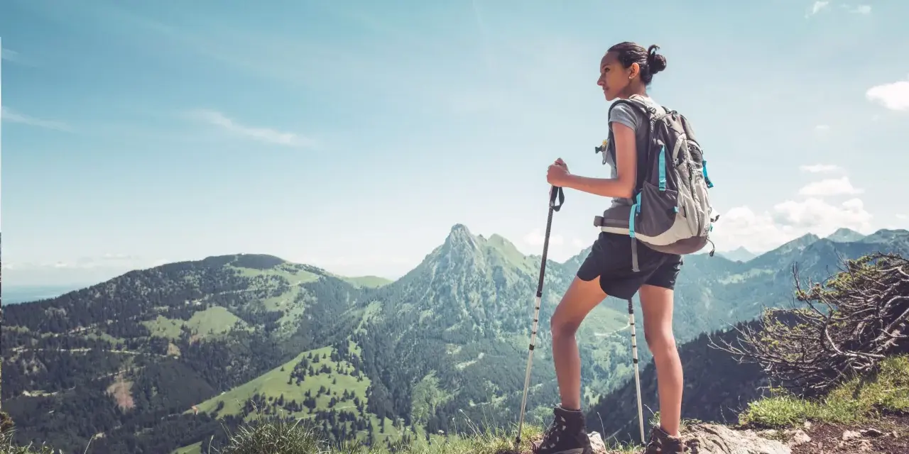Dziewczyna z plecakiem i kijkami do trekkingu podziwia górski krajobraz. To jest właśnie hiking – przygoda na łonie natury.