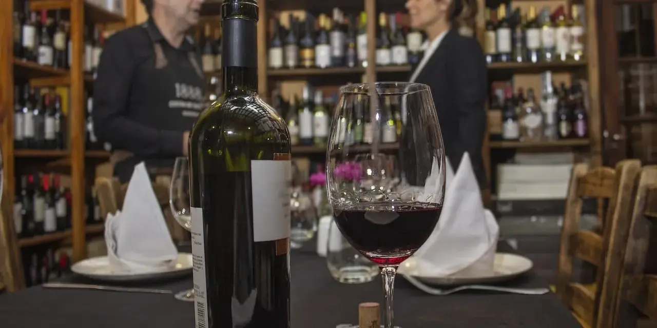 Winiarnia, butelka i kieliszek czerwonego wina na stole. Zastanawiasz się, czy można przewozić alkohol w bagażu rejestrowanym?