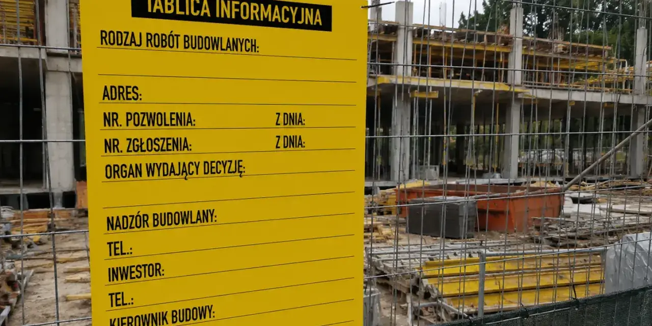 Żółta tablica informacyjna budowy z danymi o pozwoleniu, adresie i kontaktach. W tle widać konstrukcję budynku.