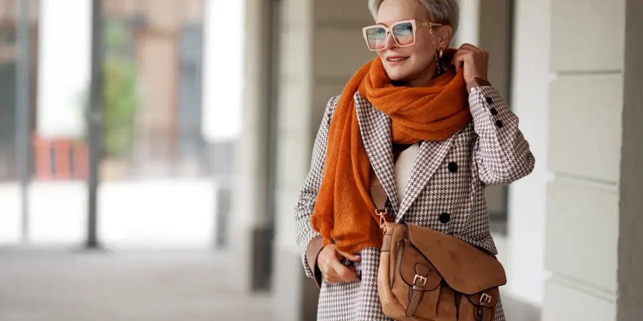 Elegancka kobieta w płaszczu w drobną kratę i pomarańczowym szalu. Czy krata pogrubia? Ten styl pokazuje, że niekoniecznie!