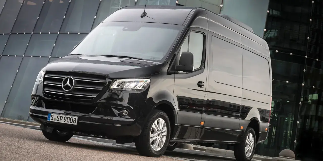Czarny furgon Mercedes-Benz Sprinter stoi przed nowoczesnym budynkiem z przeszkloną fasadą.