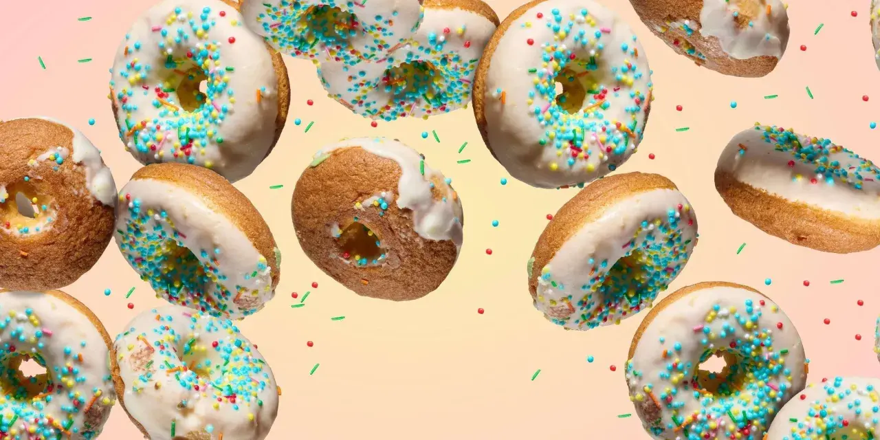 Bunte Donuts mit weißer Glasur und Streuseln schweben im Bild. Ein köstliches Rezept für selbstgemachte Donuts.