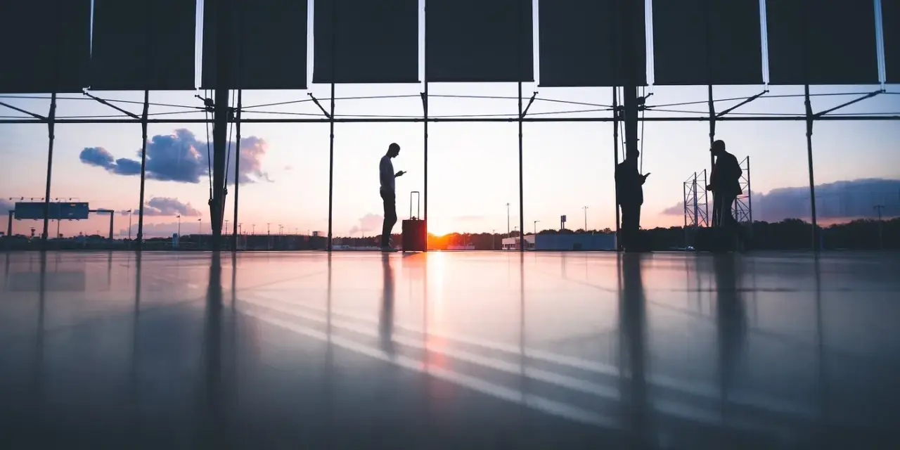 Sylwetki ludzi z bagażami czekają na lotnisku o zachodzie słońca. Czyżby to był kolejny przypadek overbookingu Ryanair?