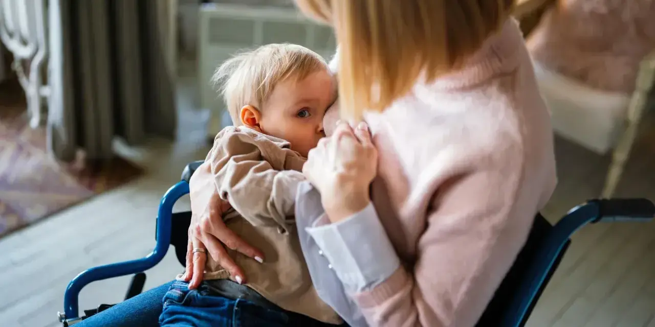Mama w wózku inwalidzkim karmi piersią dziecko. Wkrótce nadejdzie czas, jak odstawić dziecko od karmienia piersią, ale teraz liczy się bliskość.