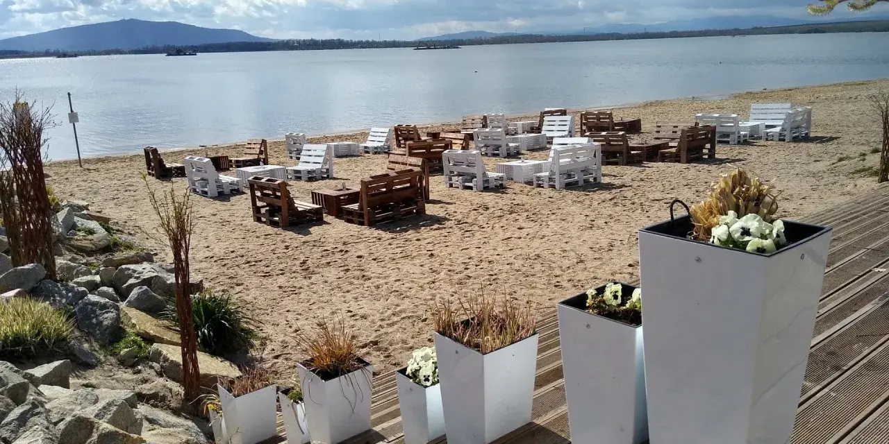 Plaża nad mietkowym zalewem z meblami z palet. W oddali góra i jezioro.