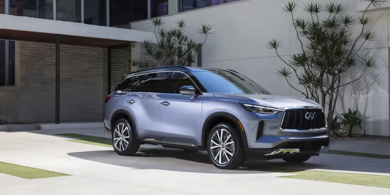Elegancki, srebrny infiniti samochód zaparkowany przed nowoczesnym budynkiem z kamienną fasadą i dużymi oknami.