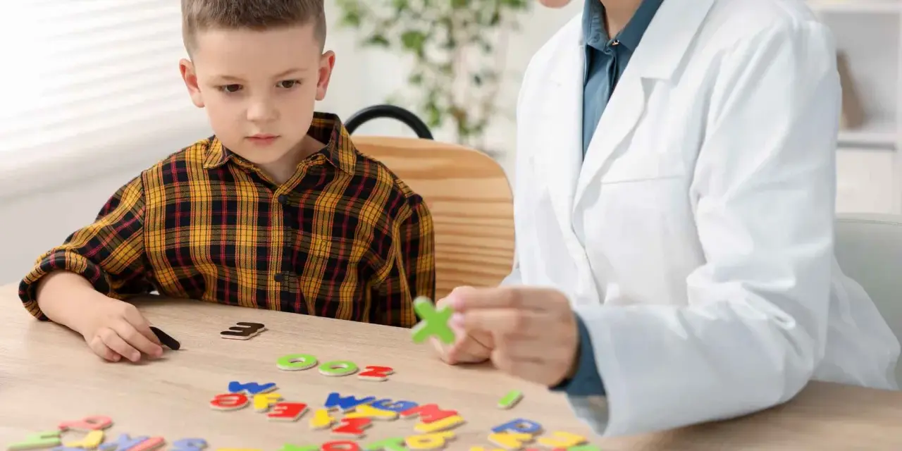 Chłopiec z dysleksją układa litery z terapeutką. Czy dysleksja to choroba? Terapia pomaga w nauce.