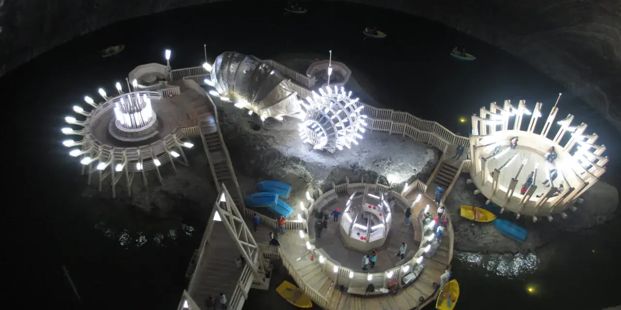 Podziemne jezioro w **Salina Turda** z łódkami i oświetlonymi platformami.