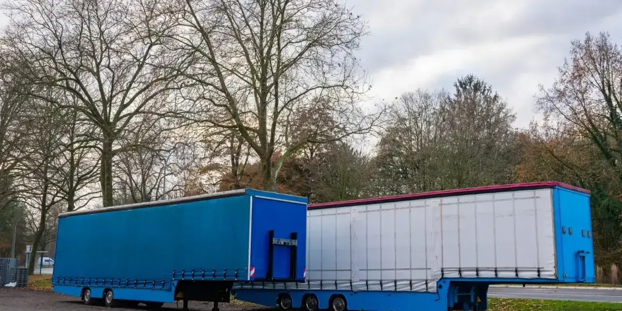 Dwa naczepy ciężarowe, jedna niebieska, druga biała, stoją obok siebie. Symbolizują one dynamiczną branżę TSL.
