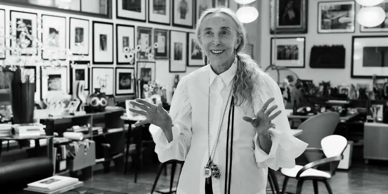Donna elegante con camicia bianca, un'icona di stile che incarna la moda di Milano. Le sue mani aperte raccontano storie di creatività e design.