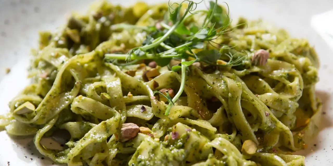 Makaron tagliatelle z zielonym sosem pesto, posypany pistacjami i udekorowany kiełkami.