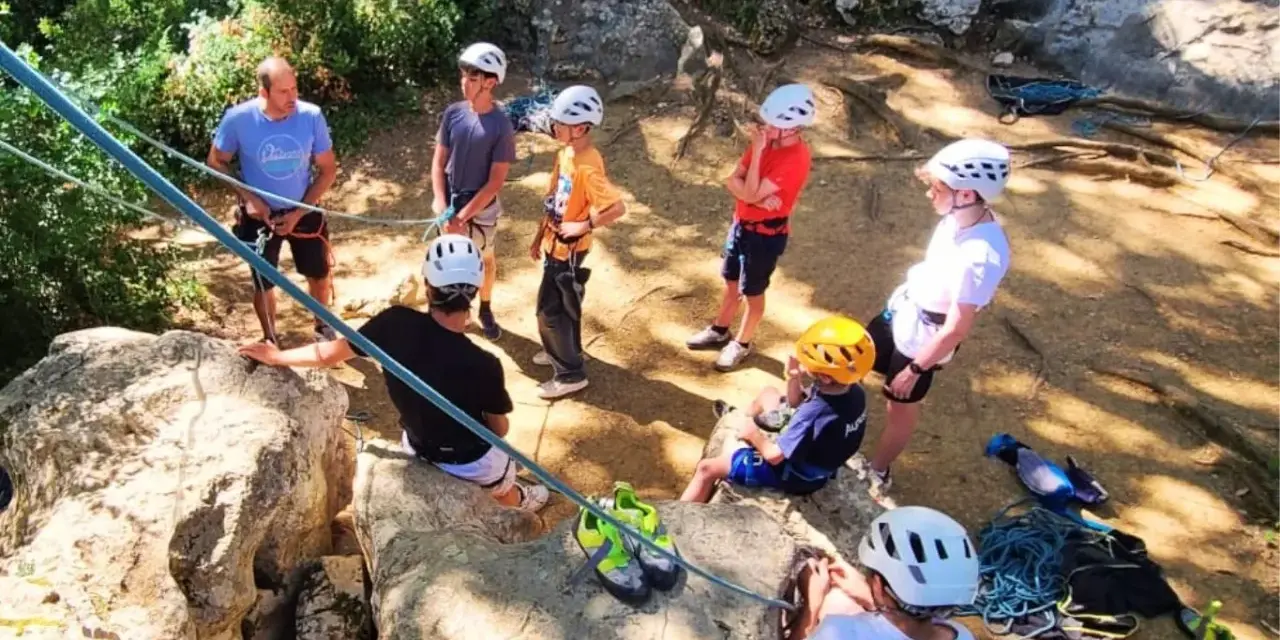 Des jeunes en pleine colonie de vacances escalade, casques blancs et jaunes, prêts pour l'aventure sur les rochers.