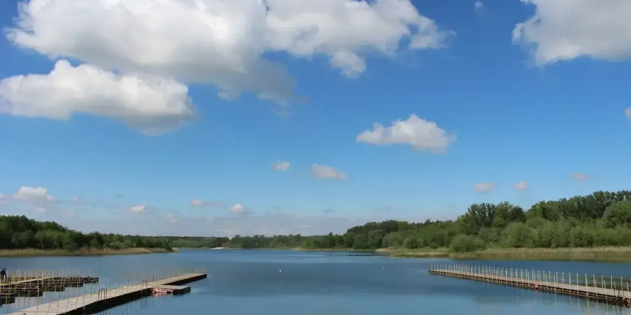 Piękny dzień nad jeziorem Wilczyńskim. Piaszczysta plaża, drewniane pomosty i błękitne niebo z białymi chmurami zapraszają do wypoczynku.
