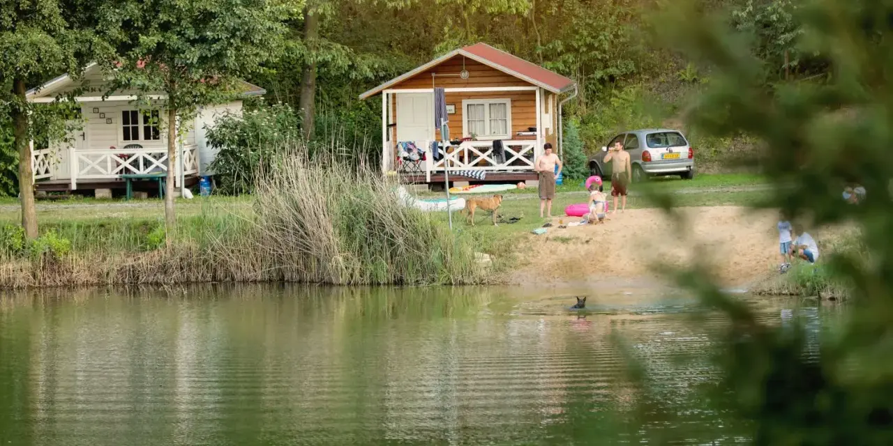 Rodzina odpoczywa nad jeziorem w malowniczym miejscu. Dzieci pluskają się w wodzie, a dorośli relaksują się na plaży przy domkach kempingowych. To idealne miejsce na rodzinne wakacje, prawdziwa **camping forteca** spokoju i radości.