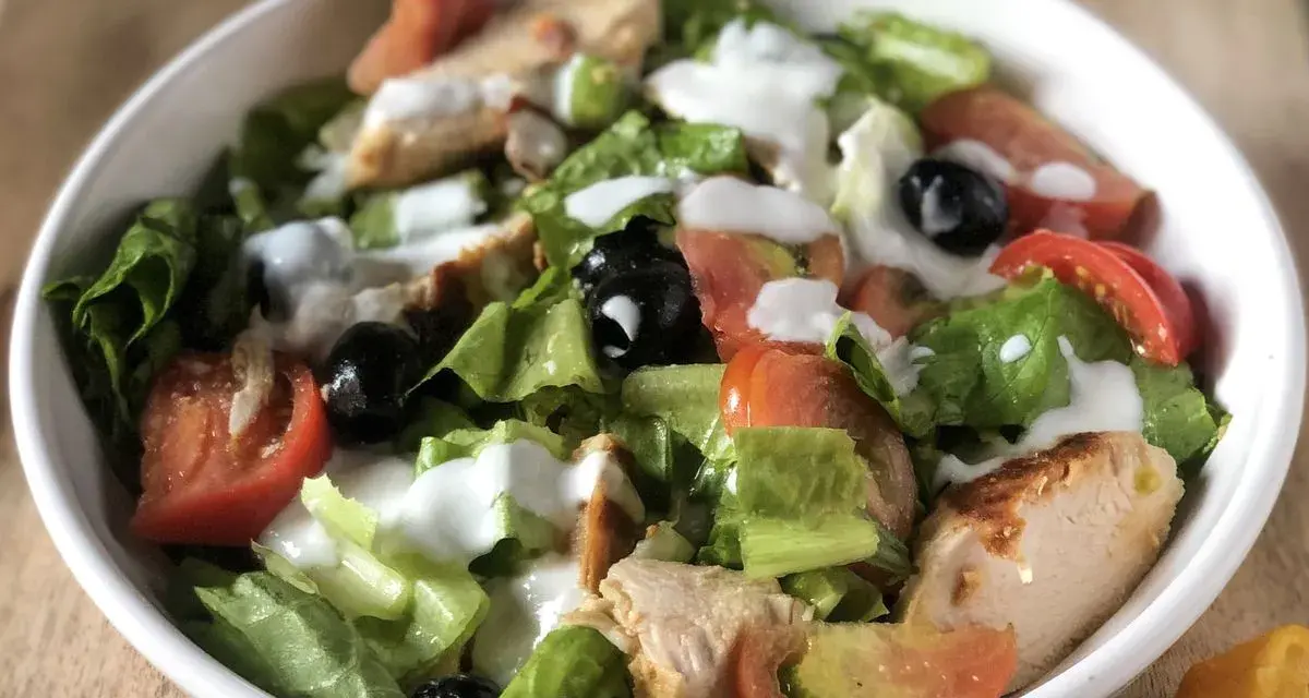 Insalata di pollo ricetta: lattuga croccante, pomodoro, olive nere e succulenti pezzi di pollo, condita con una cremosa salsa bianca.