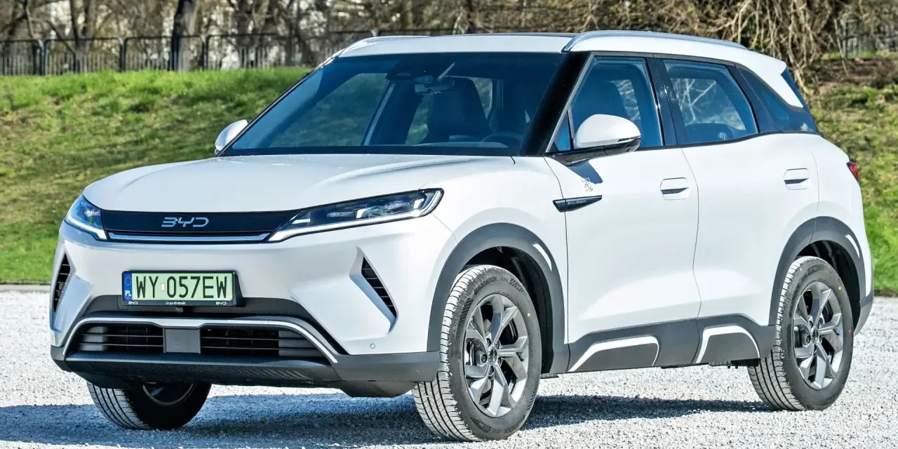 Biały SUV z logo BYD, jeden z chińskich samochodów elektrycznych, zaparkowany na żwirowej nawierzchni.