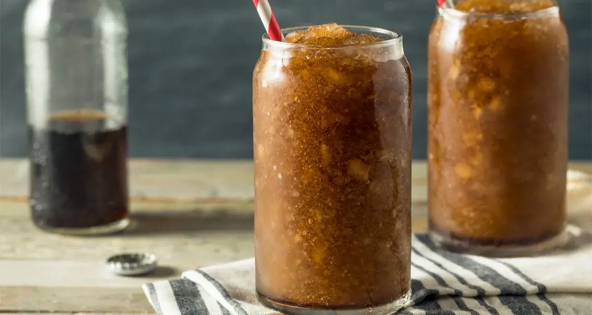 Zwei Gläser mit erfrischendem Cola Slush Eis, bereit zum Genießen. Eine Flasche Cola steht daneben.