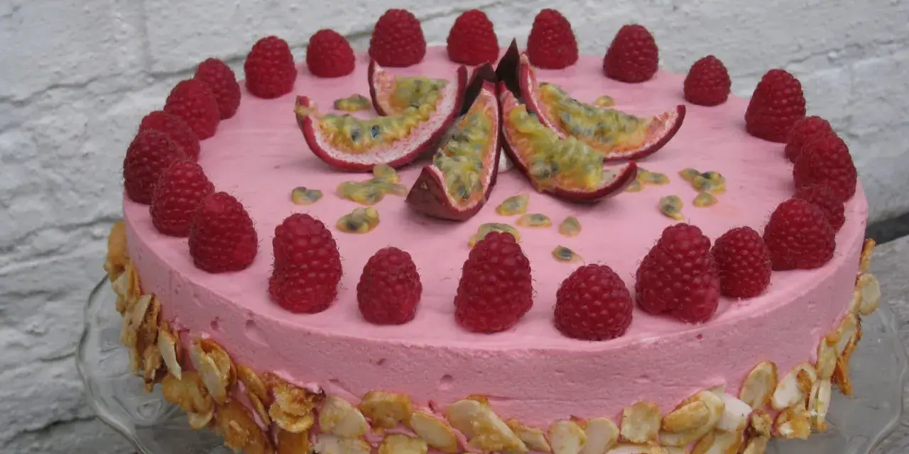 En rosa hallonmousse tårta dekorerad med färska hallon och passionsfrukt. Kanterna är täckta med rostade mandelflagor.