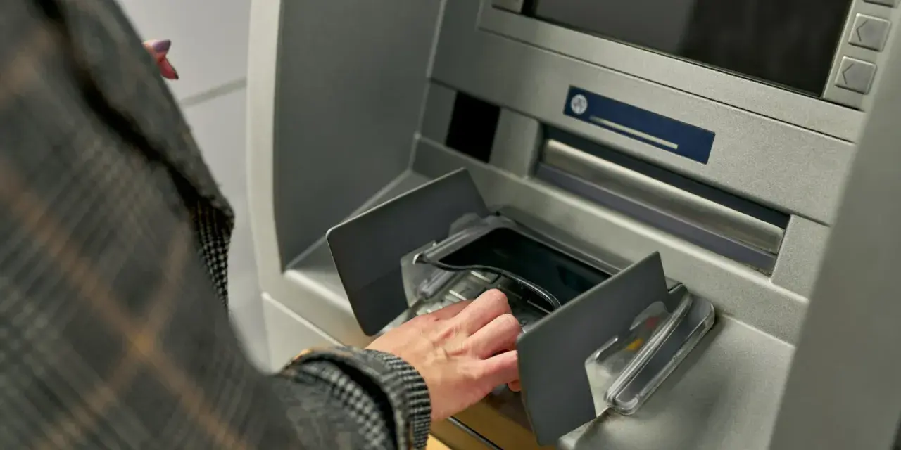 Dłoń w rękawie w kratę wkłada pieniądze do bankomatu. Szybka jednorazowa wpłata gotówki do banku.