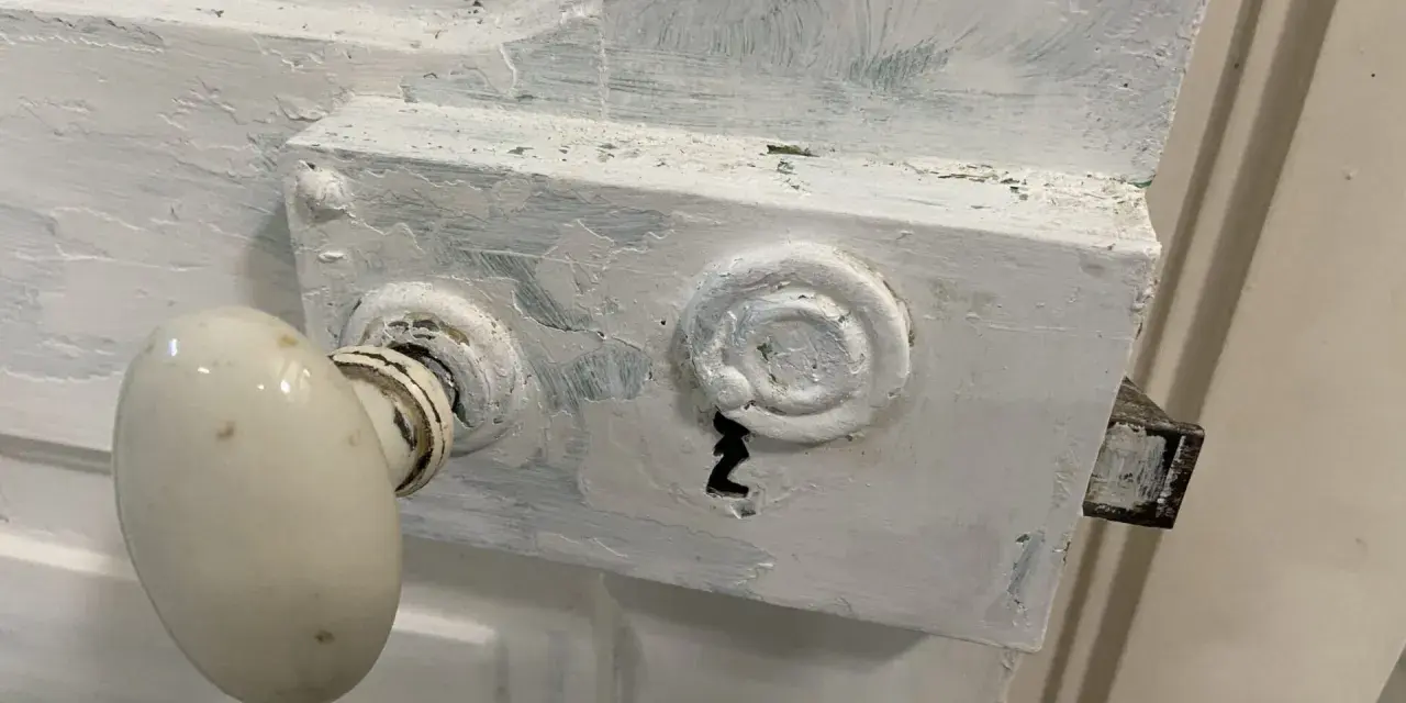 Poignée de porte ancienne recouverte de peinture blanche écaillée, prête à être nettoyée.