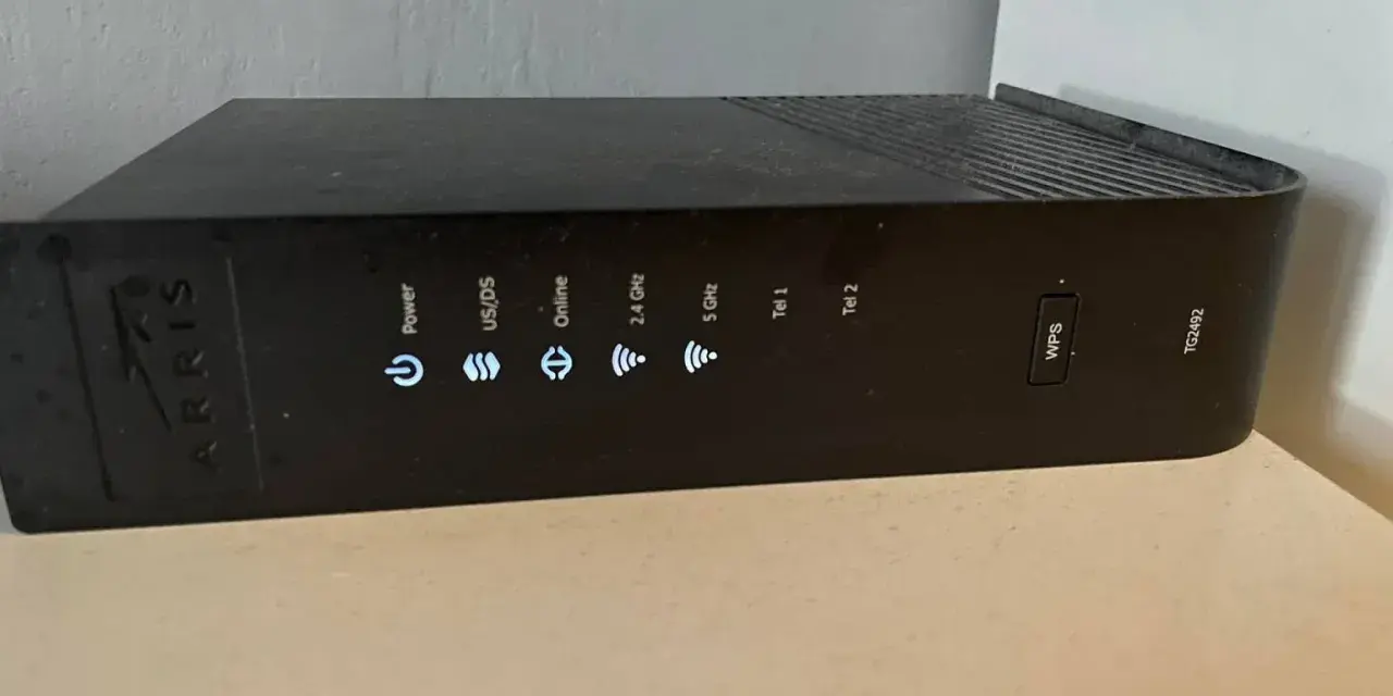 Czarny router Arris TG2492 z widocznym przyciskiem WPS i wskaźnikami stanu: Power, US/DS, Online, 2.4 GHz, 5 GHz, Tel 1, Tel 2.