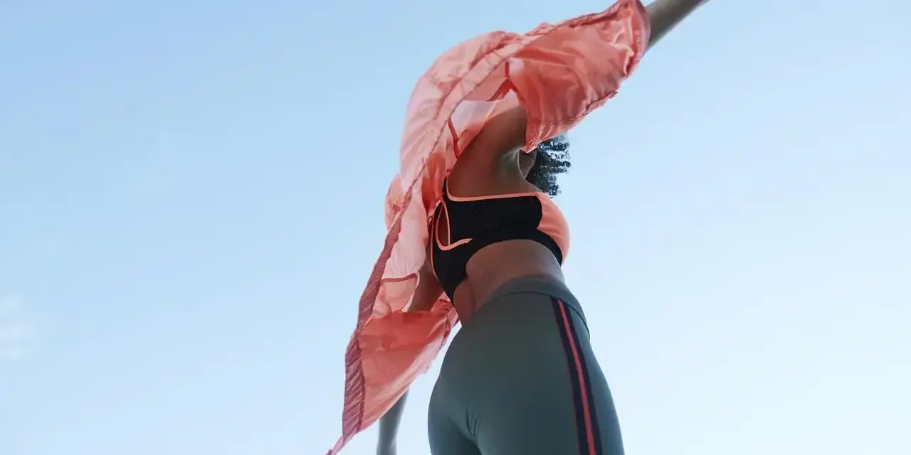 Kobieta w sportowym stroju, w tym legginsach z materiału spandex, tańczy na tle błękitnego nieba.