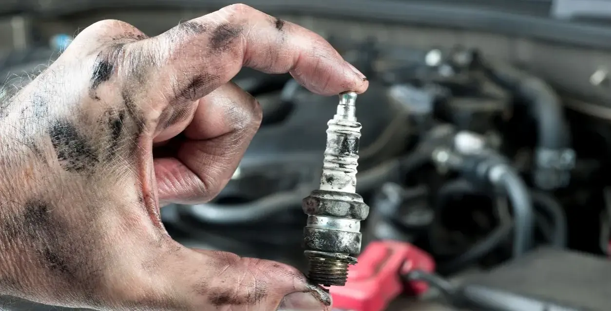 A mechanic's greasy hand holds a used spark plug, a reminder that many cars still have spark plugs for ignition.