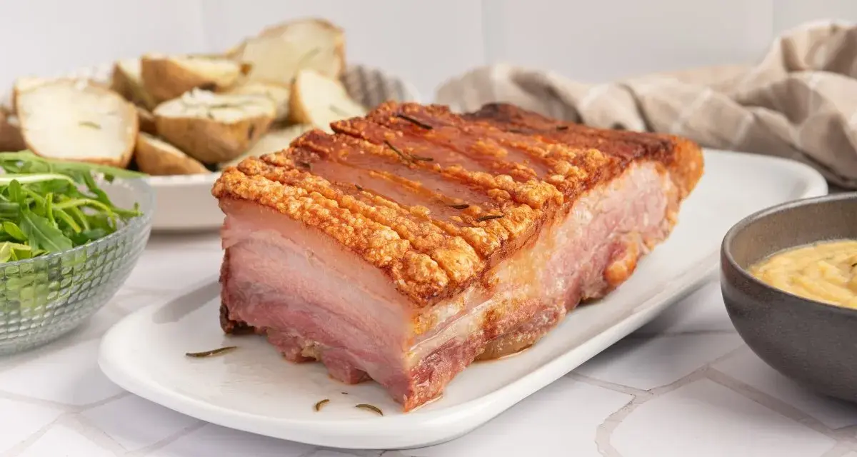 Panceta de cerdo al horno con piel crujiente, acompañada de patatas asadas y ensalada.