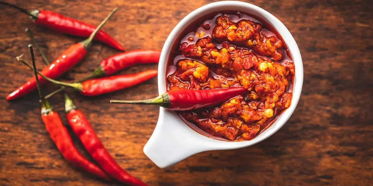 Scharfes Essen stillen: Eine Schale mit feuriger Chilisauce und frischen roten Chilis auf einem Holztisch.