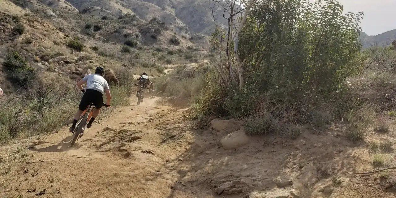 Dust flies as cyclists tackle a rugged trail, enjoying mountain biking in Los Angeles.