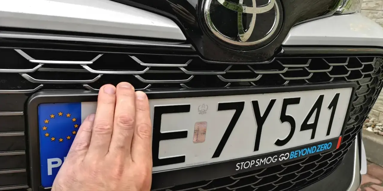 Dłoń zasłania część tablicy rejestracyjnej E 7Y541. Pod nią widoczny jest napis "STOP SMOG GO BEYOND ZERO".