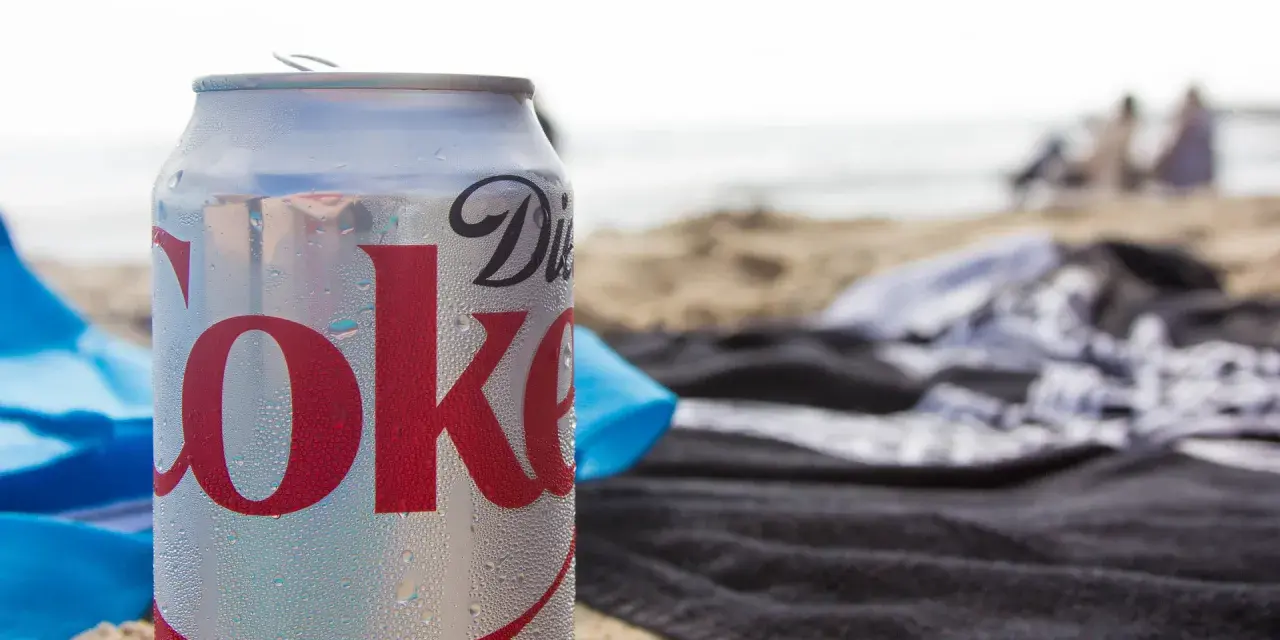En burk Diet Coke på stranden, perfekt för den som vill undvika socker och hantera diabetes. Sukralos i drycken gör den till ett sockerfritt alternativ.