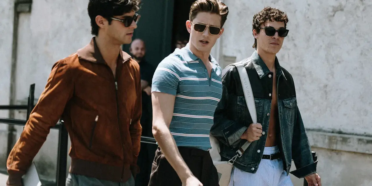 Tre uomini camminano insieme, uno con giacca marrone, uno con polo a righe e uno con giacca di jeans. Un look uomo di stile.