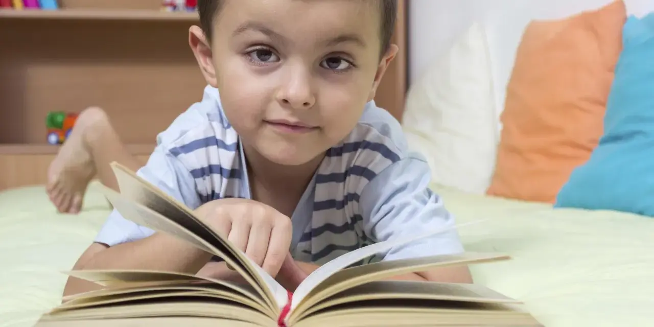 Chłopiec leży na łóżku z otwartą książką. To świetny sposób, jak zachęcić dziecko do czytania.