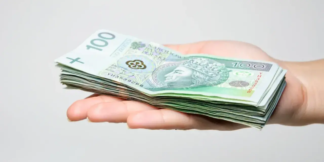 Stos banknotów 100 zł na dłoni, symbolizujący środki do zgłoszenia spadku do urzędu skarbowego.
