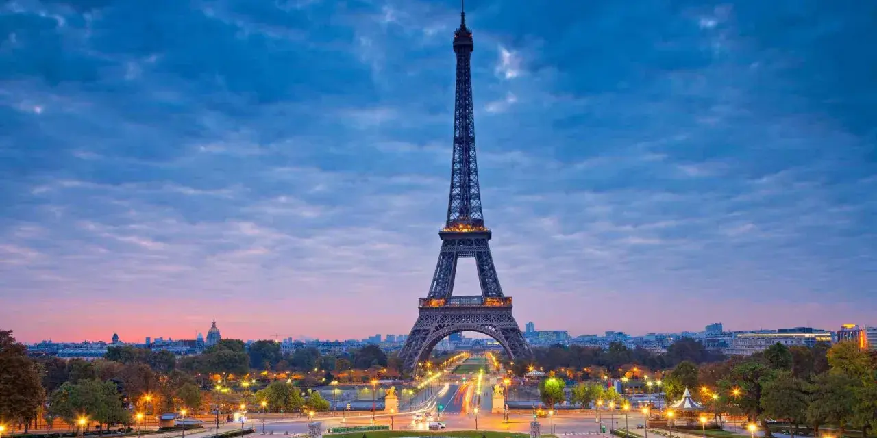 Torre Eiffel iluminada al atardecer, uno de los iconos franceses más reconocidos, con el cielo azul y nubes rosadas.