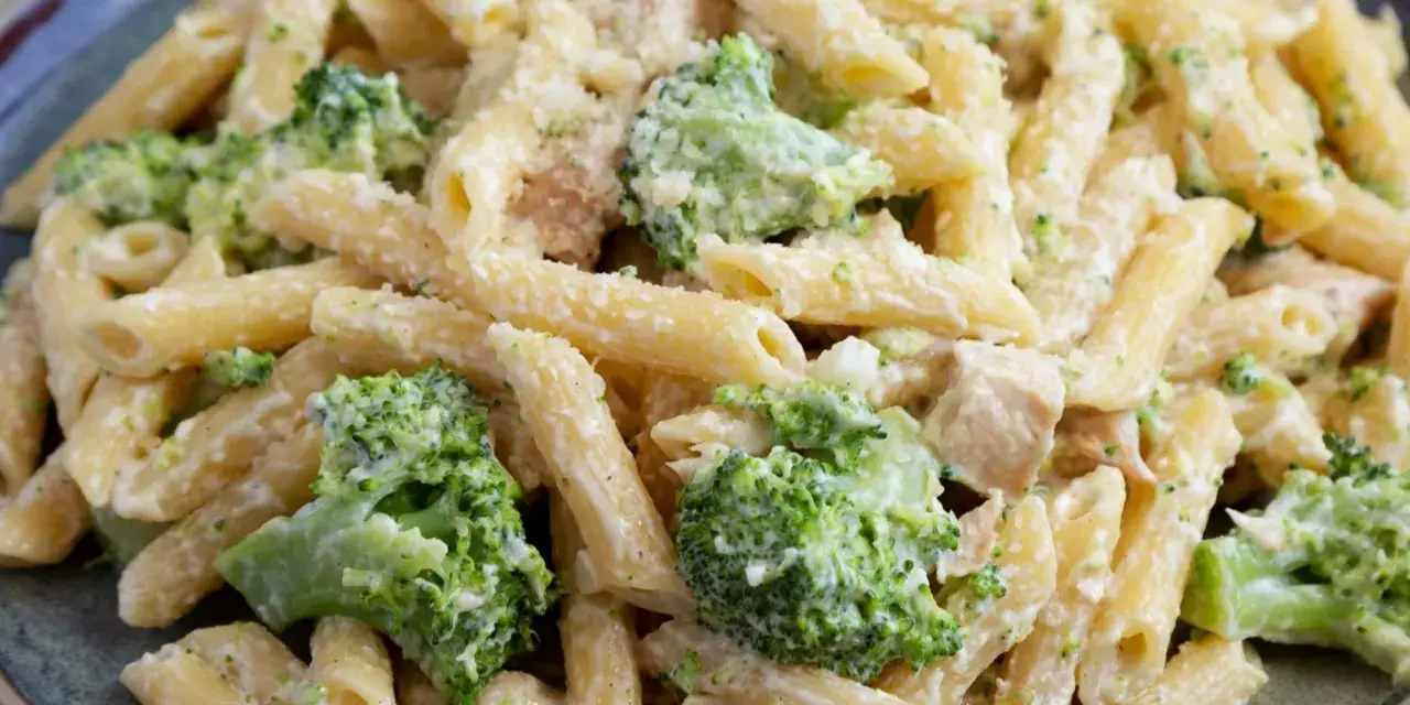 Penne z kurczakiem i kremowym sosem, obficie posypane zielonymi różyczkami brokułów. Pyszne makaron z brokułami na talerzu.