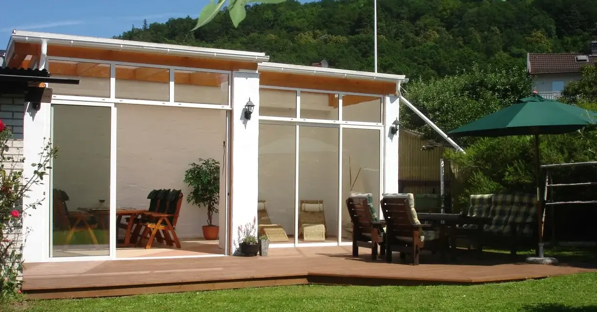 En modern glasveranda med trädgårdsmöbler och parasoll. Perfekt uteplats inspiration för soliga dagar.