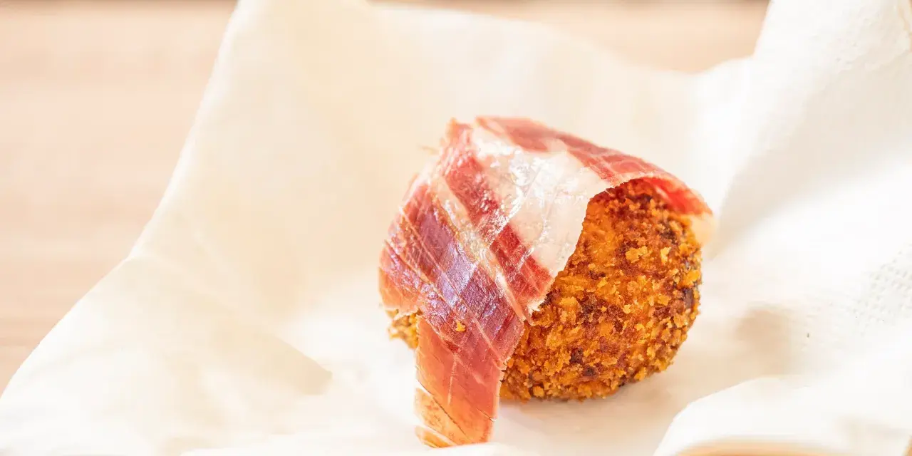 Croqueta dorada con jamón ibérico, servida sobre papel blanco.