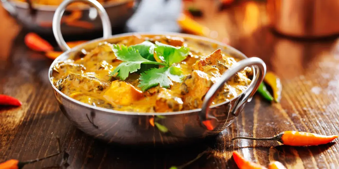 Ein cremiges Curry, garniert mit Koriander, umgeben von bunten Chilis. Ein Genuss für Liebhaber indischer Gerichte.