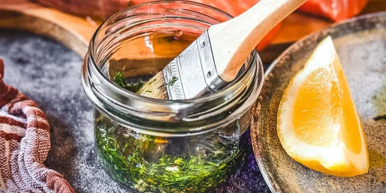Marinade mit Kräutern und Zitrone bereit, um den Lachs zu verfeinern. Ein Pinsel liegt in der Glasflasche.