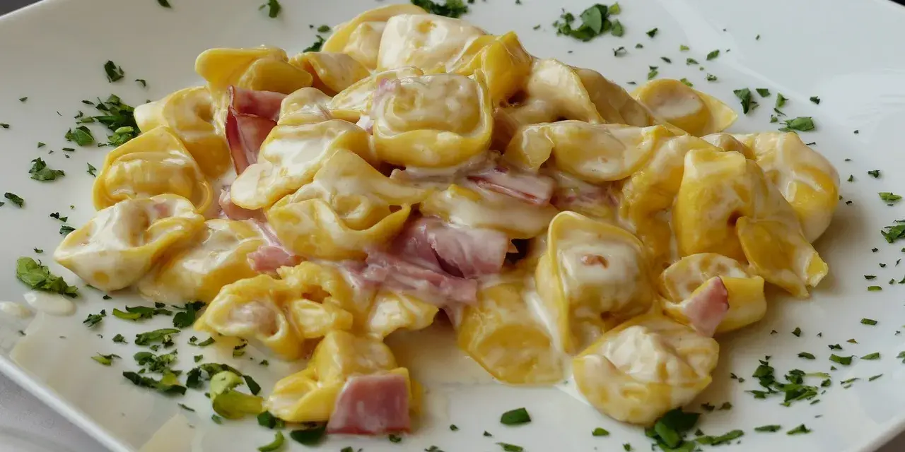 Tortellini panna e prosciutto, un piatto cremoso e saporito, guarnito con prezzemolo fresco su un piatto bianco.